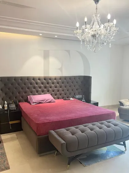 A grand bedroom featuring a bed with an extra-tall, tufted headboard in dark grey. Paired with a matching bench and a crystal chandelier, this room is the definition of opulent comfort.