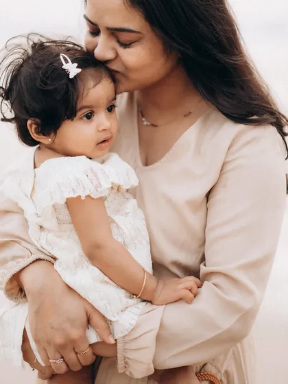A mother gently kisses her baby's forehead in a soft, warm light. This close-up captures the quiet tenderness and deep affection in a mother-child portrait.