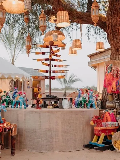 A beautiful decor detail from the Mehendi, featuring a favor station with colorful puppets and local crafts under a tree adorned with lanterns.