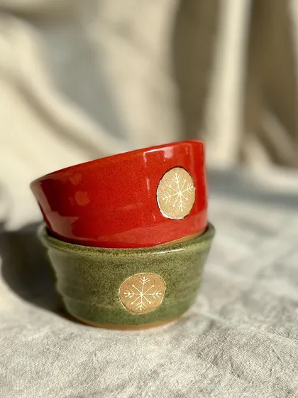 A pair of small bowls in festive red and green, each with a gold snowflake emblem. These are great for serving dips or holding little trinkets.