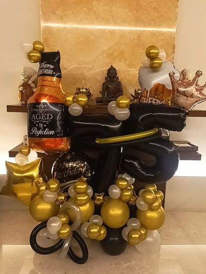 A fun and masculine balloon bouquet, perfect for a man's birthday. It features a whiskey bottle foil balloon, a crown, and a black and gold color scheme.