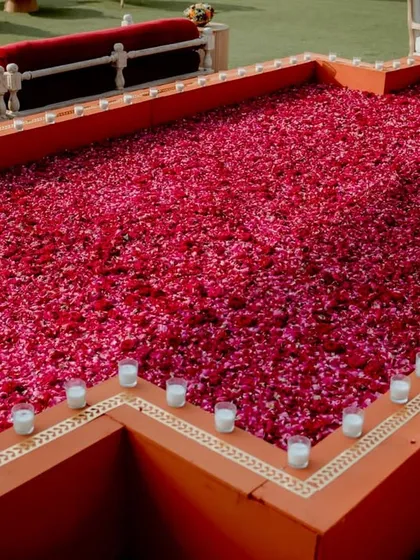 A stunning detail from a traditional wedding: a large platform filled with a bed of vibrant red and pink flower petals, surrounded by candles. A simple concept executed on a grand scale for a powerful romantic statement.