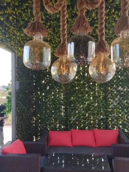 A comfortable lounge area created within a green trellis. The space is made intimate with an artificial leaf roof and walls, and features a unique rope and bulb chandelier.