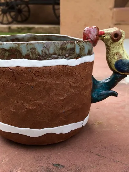A whimsical, creative cup with a bird forming the handle. The bird appears to be taking a sip from the cup, adding a playful narrative to a functional object.