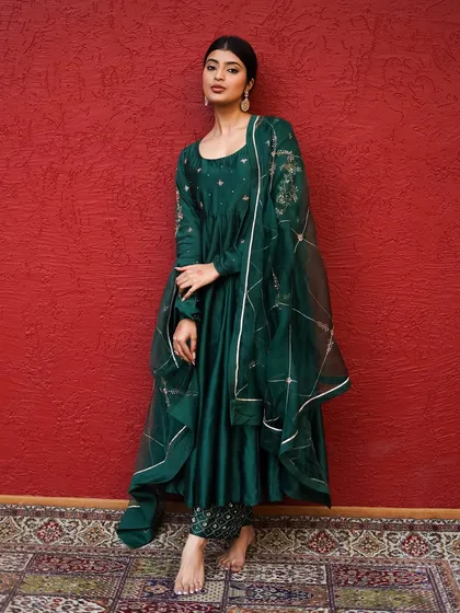 I love making colors speak. Here, the deep emerald green of the Anarkali suit is the hero, set against a rich red backdrop. This is a perfect example of a lookbook shot that highlights the garment's regal quality and intricate embroidery.