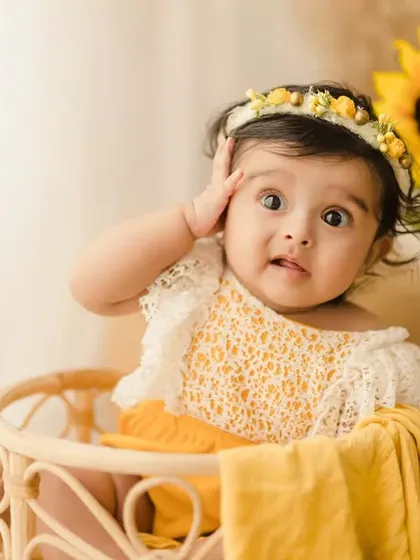 A cute and funny moment from a 6-month sitter session. The baby girl makes a surprised face while sitting in a wicker basket, showing off her playful side.