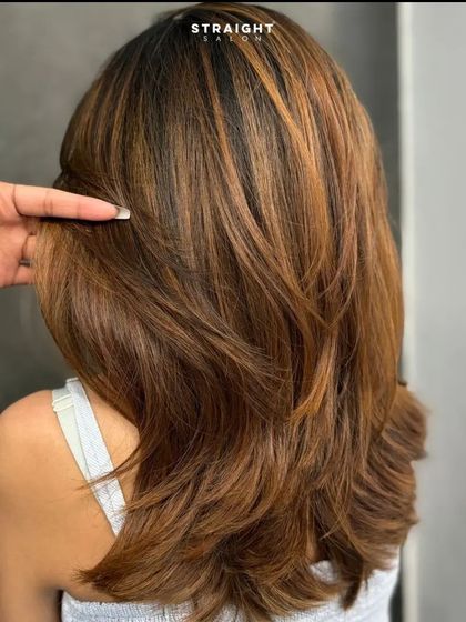 A stylist's hand shows the texture and health of the layered hair.