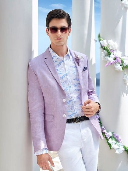 A summer occasion look for Louis Philippe, featuring a lavender linen blazer paired with a floral shirt and crisp white trousers. The styling, complete with sunglasses, creates a relaxed yet sophisticated aesthetic for a destination wedding.