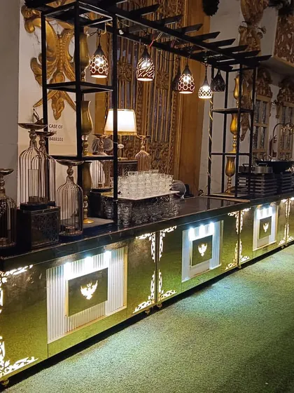 Our black and gold themed buffet counter, featuring an overhead structure with hanging lamps and decorative elements. This design adds height and drama to the food display, perfect for a glamorous evening affair.