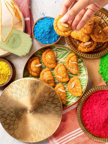 A hand reaching for a piece of my freshly made Ghujiya from a festive tin. It’s a sweet, crunchy bite that is simply irresistible during Holi festivities.