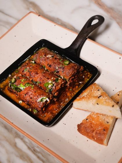 My smoky and spicy Mutton Seekh Kebabs arrive sizzling in their own juices, served in a cast-iron pan with soft, house-made bread for mopping it all up.