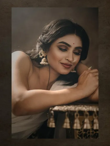 A close-up portrait where the model rests her head on a decorative table. The focus is on her serene expression and the delicate details of her nose ring and makeup.