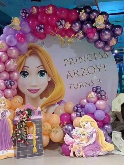 An elaborate Rapunzel themed party with a large custom backdrop, character cutouts, and a balloon arch in shades of purple and pink.