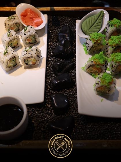 Two varieties of sushi rolls, one with green tobiko and the other with black sesame, are beautifully presented on white platters with decorative stones, showcasing our creative buffet displays.