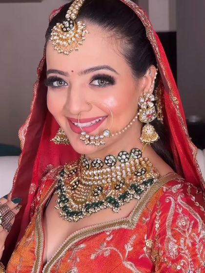 A happy bride showcasing her complete look. This image highlights the beautiful combination of a traditional red and orange lehenga with a contrasting green and black kundan jewellery set.