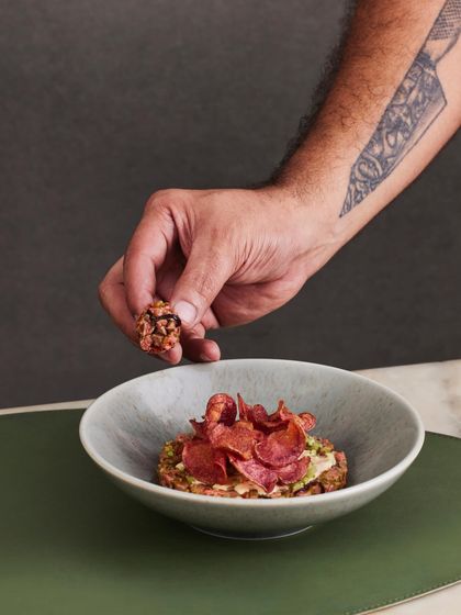 The chef's hand presenting a perfect bite of the Seared Steak Tartare on a crispy chip.