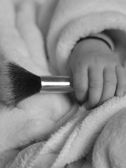 A detail shot from the spa theme, focusing on the baby's tiny hand holding a makeup brush. This black and white image highlights the adorable contrast in scale.