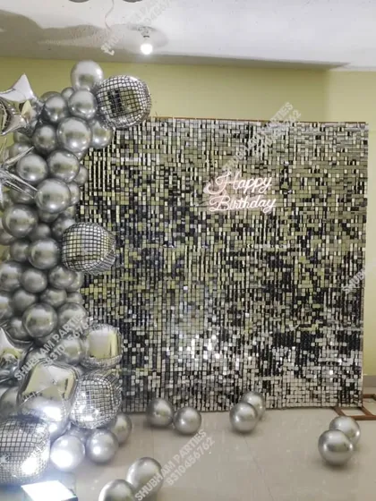 Make your birthday unforgettable with a glamorous silver sequin wall backdrop. This party setup creates a perfect photo booth, featuring a cascade of chrome silver balloons, disco balls, star-shaped foil balloons, and a bright "Happy Birthday" neon sign.