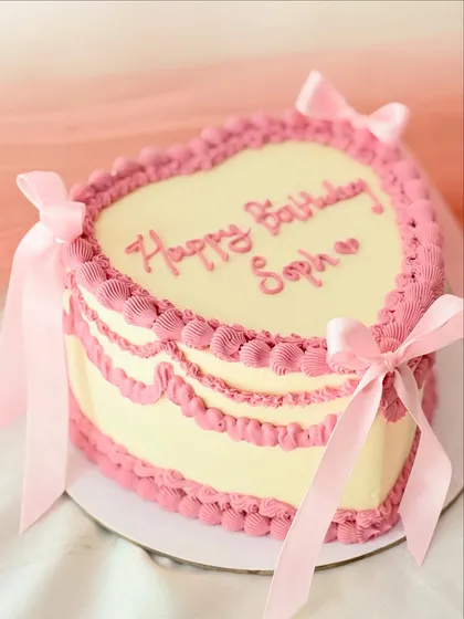A classic vintage heart-shaped cake for a special birthday. This design features intricate pink Lambeth-style piping and delicate satin bows, bringing a touch of romantic nostalgia to the celebration.