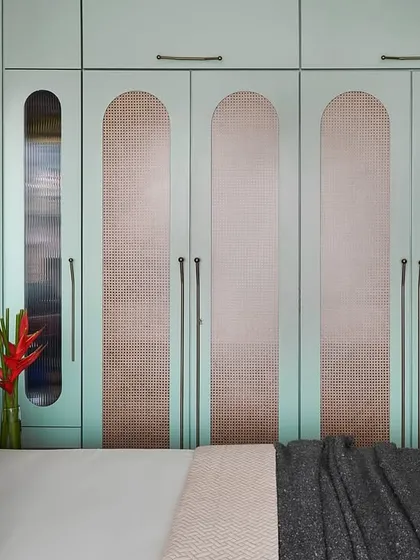 The wardrobe in the master bedroom features sage green shutters with cane inlays and capsule-like forms. This custom design adds a unique geometric pattern and accent to the room.