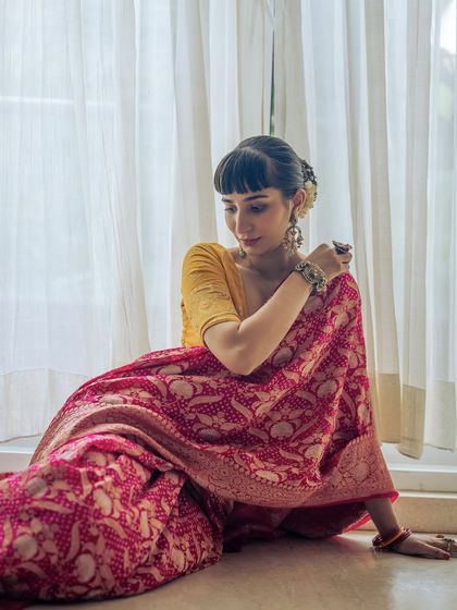 A quiet moment in the beautiful Banarasi Bandhani saree. The soft light from the window highlights the rich texture and deep pink hue of the handcrafted textile.