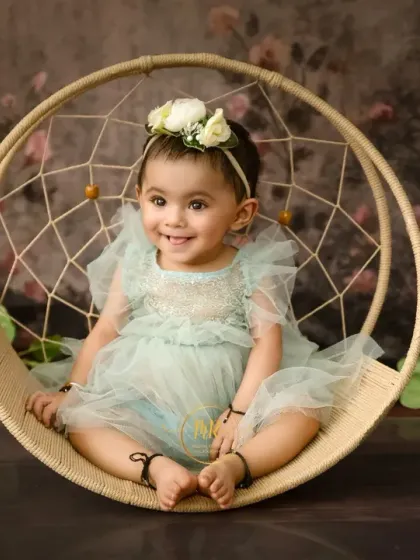 A smiling baby girl sits in a dreamcatcher-style swing, a popular prop for sitter sessions.