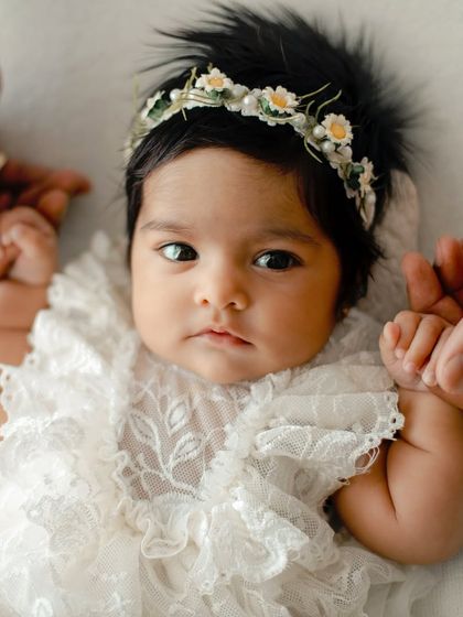 A detailed shot of a baby girl in a lace dress and floral headband. I focus on capturing the textures and her serene expression.