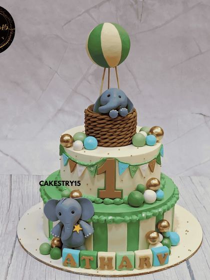 A joyful two-tier elephant-themed cake for a first birthday. This 3kg mixed fruit cake features a green and white color scheme with an elephant in a hot air balloon.