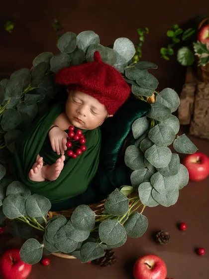 Our little artist is dreaming of his next masterpiece. This overhead shot shows the baby surrounded by red apples and green leaves, creating a rich, artistic composition.