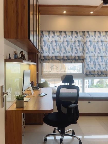 A full view of the home office setup, with a spacious desk, ergonomic chair, and a large window with patterned blinds that fills the space with light.