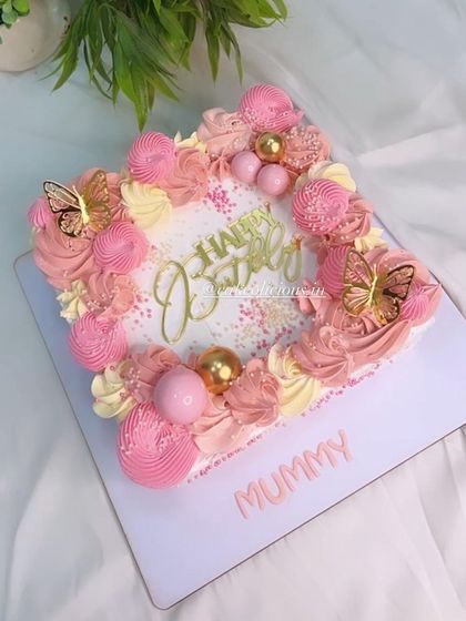 Sheet cakes are a great option for large gatherings as they are easy to cut and serve. This square sheet cake is beautifully decorated with pink piped frosting, golden butterflies, and decorative balls.