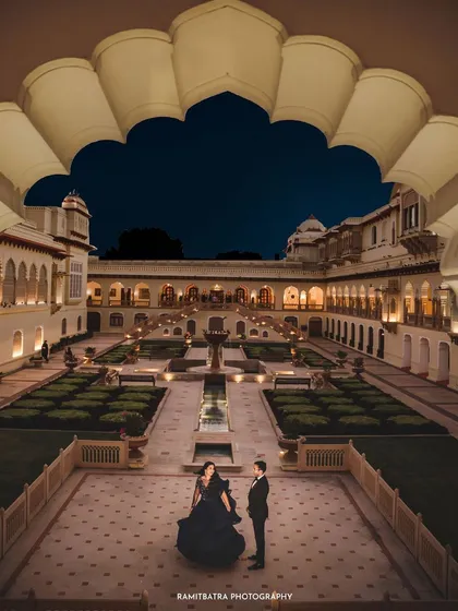 Under the night sky, the Rambagh Palace in Jaipur glows, providing a regal backdrop for a couple's portrait. This image speaks to the timeless elegance and romance of a palace wedding, a fairytale brought to life.