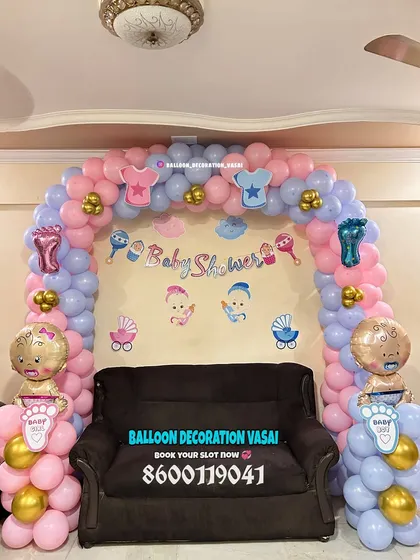 A cute and simple baby shower theme for a home setting. The balloon arch is decorated with cutouts of baby clothes and rattles, and the foil baby balloons on the sides add a playful touch.