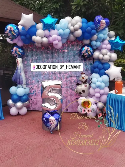 A Frozen theme birthday setup featuring a shimmering blue sequin wall. The balloon garland in shades of blue, white, and lilac is accented with character foil balloons of Elsa and Olaf, and a large number '5' prop.