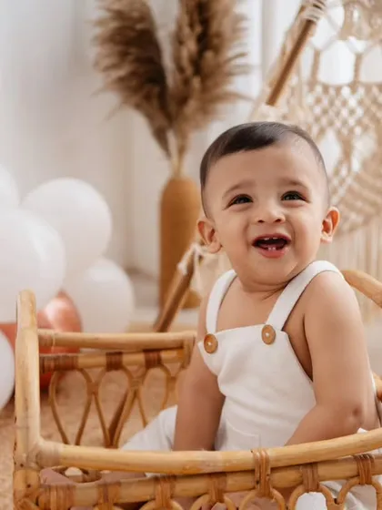 Such a happy boy in my boho studio! This little one is sitting in a wicker basket, surrounded by balloons and a teepee, celebrating his first birthday in style.