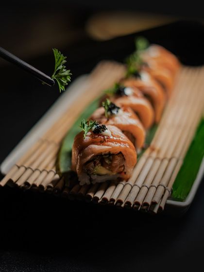 A delicate dance of flavours and finesse. We invite you to indulge in our finest Japanese sushi, like this seared salmon roll, garnished with fresh parsley.