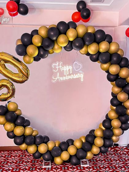 Celebrating 50 golden years together! A chic and modern circular balloon arch in black and gold, with large '50' foil balloons and a 'Happy Anniversary' neon sign, marks this incredible milestone in style.