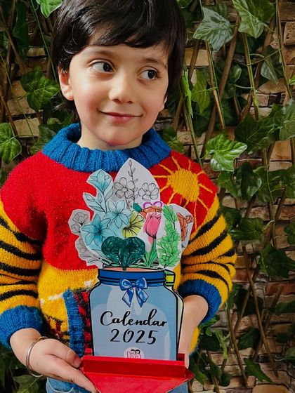 A young boy in a colorful sweater with the equally colorful calendar he crafted.