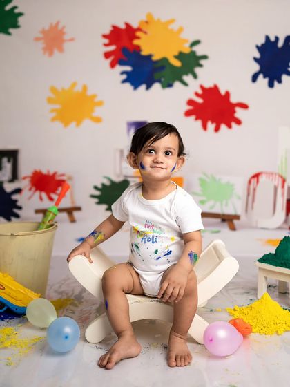 Getting ready for a colorful celebration with a Holi-themed baby photoshoot. The paint splatters on the background and his onesie add a fun, messy touch.
