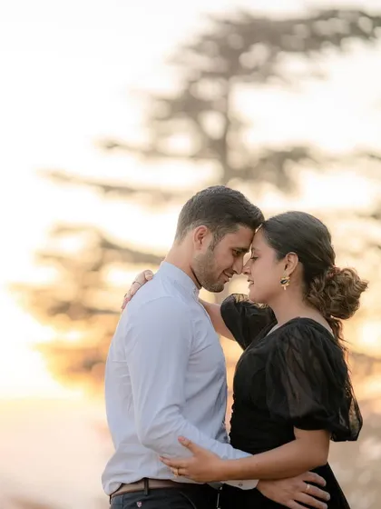 A couple embraces against the soft, hazy light of a sunset in the hills, creating a warm and romantic silhouette effect.