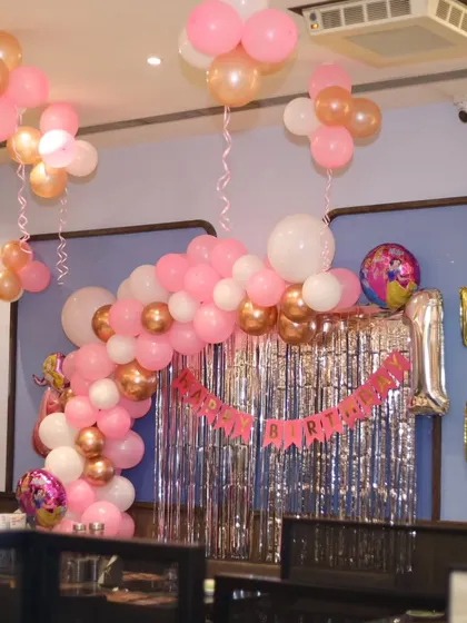A princess-themed birthday setup with a pink and rose gold balloon arch, silver fringe curtain, and name spelled out in foil letters.
