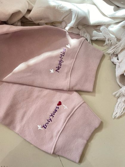 A closer look at the finished custom cuff embroidery for a couple's sweatshirt set, reading 'Truly Yours' and 'Nearly Mine'.