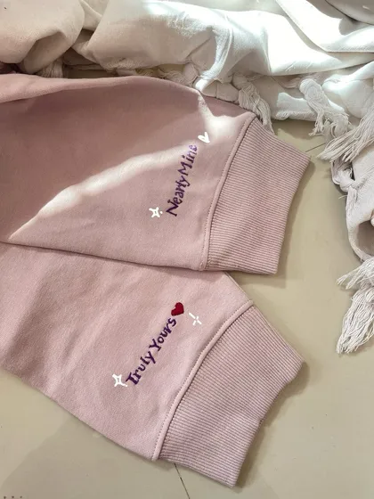 A closer look at the finished custom cuff embroidery for a couple's sweatshirt set, reading 'Truly Yours' and 'Nearly Mine'.