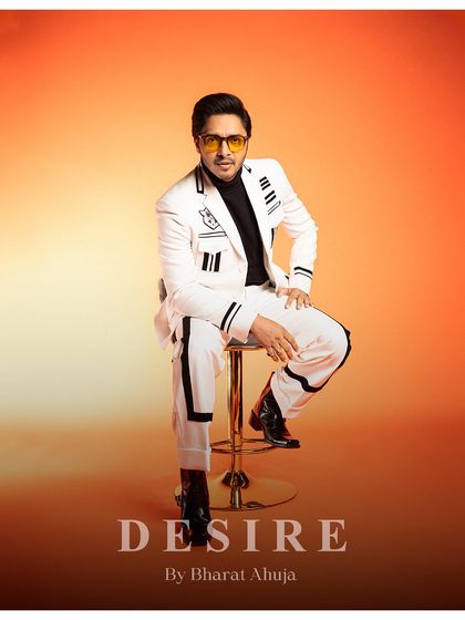 A confident, seated pose that highlights the full ensemble, from the striped jacket and trousers to the black turtleneck underneath.