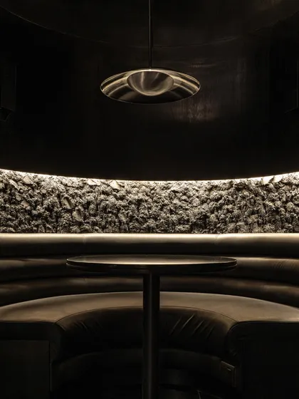 An intimate booth set against a wall of rough, dark stone. The design uses texture to create warmth and interest within a monochromatic palette, ensuring the space feels rich and layered.