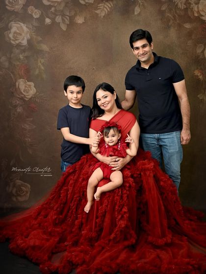 A beautiful family portrait with a classic, painted backdrop. The rich red of the mother and daughter's dresses stands out beautifully, creating a warm and inviting image.