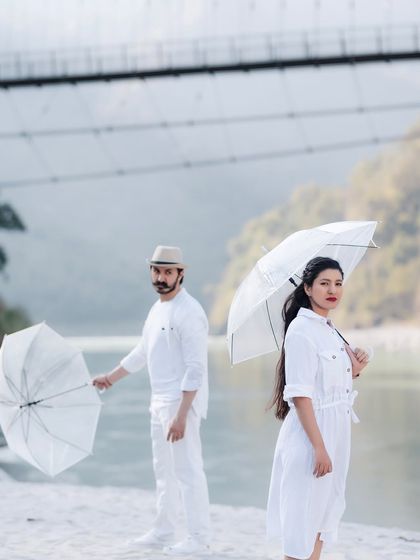 A stylized, retro-inspired shot with the couple in all-white outfits holding umbrellas on the riverbank. This shows how we can play with different themes and props.