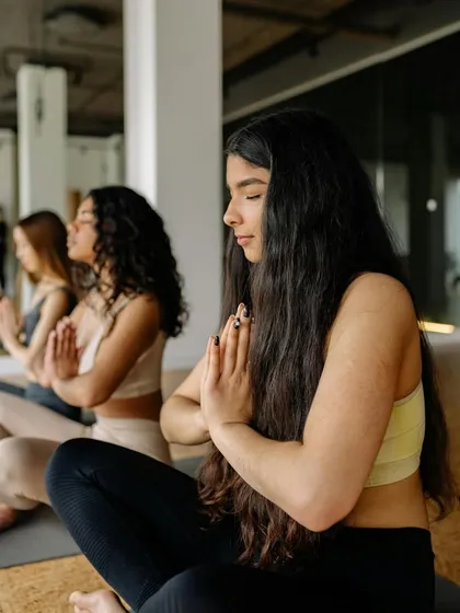 A group of students in meditation, with hands in Anjali Mudra. Our courses emphasize finding inner peace and balancing the mind, body, and soul.
