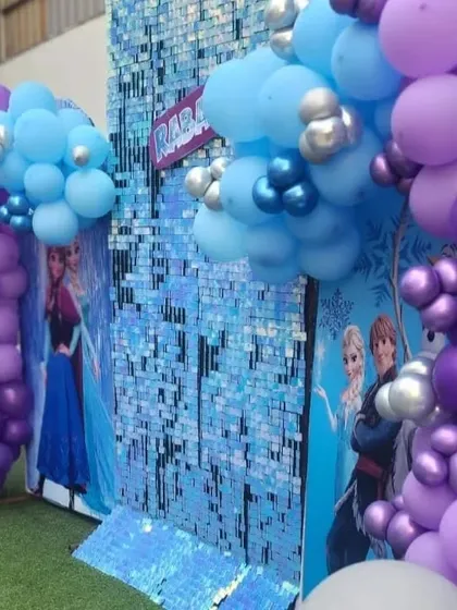 A magical 'Frozen' theme party with a shimmering sequin wall and balloon arrangements in shades of blue, purple, and silver.