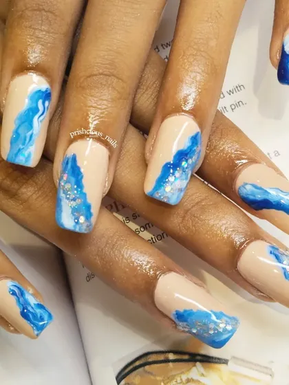 Ride the wave with these ocean-inspired nails. This design features hand-painted blue waves with silver glitter on a nude base.